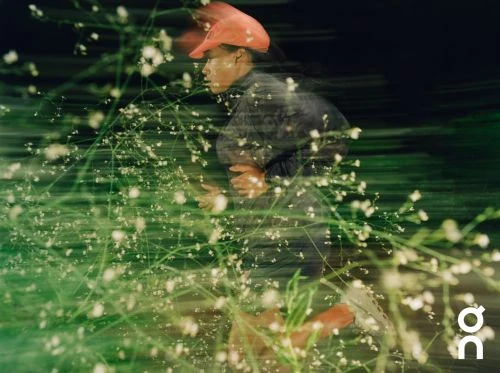 Runner in bright orange cap running past green foliage captured with long exposure motion blur