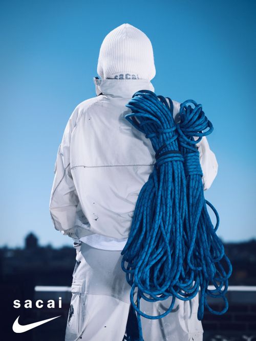 Back view of a person wearing a white beanie and jacket with a bundle of blue rope slung over the shoulder against a blue sky.