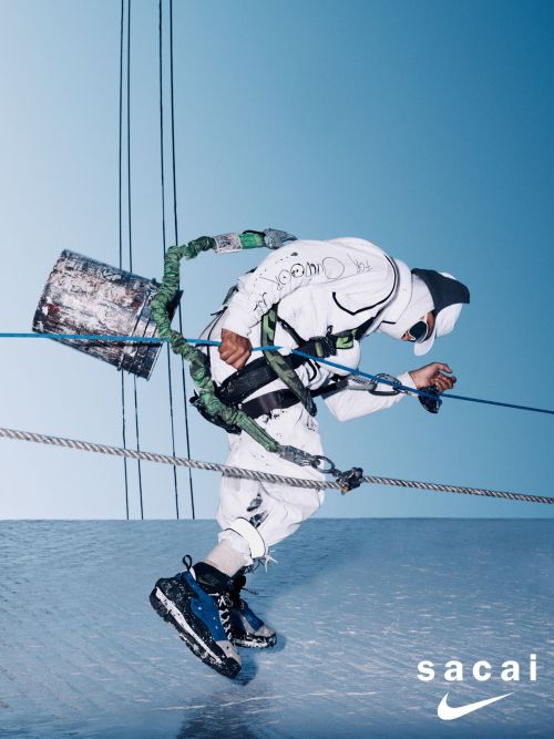 Adult wearing a white protective suit and carrying a bucket with ropes against a light blue sky, showcasing the Sacai Nike shoe brand.