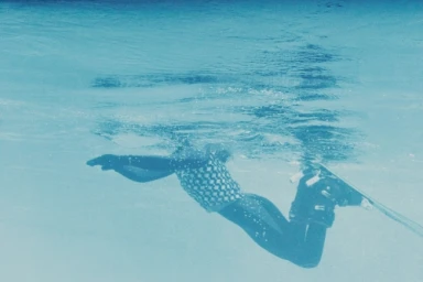 Underwater shot by Cole Barash of a swimmer wearing a checkered top and dark bottoms gliding beneath the water surface