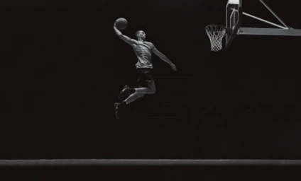 Basketball player mid-air dunking a basketball toward a hoop in a low-key black and white sports photograph