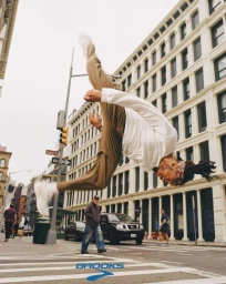 Man mid-air doing a backflip in a New York street wearing khaki trousers and a white long-sleeve shirt