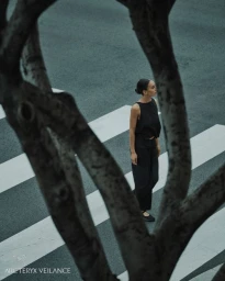 Woman in a black top and trousers standing on a zebra crossing framed by dark tree branches