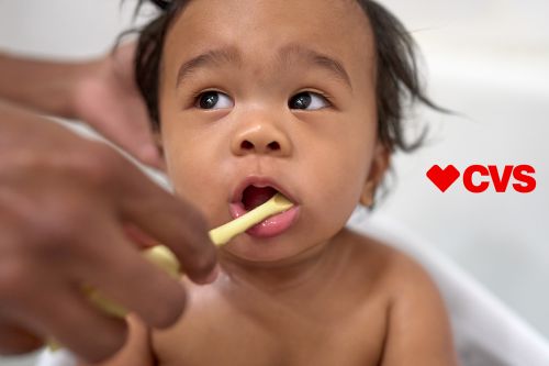 Close-up of a baby having teeth brushed by an adult, featuring an open mouth and visible CVS logo with a white background.