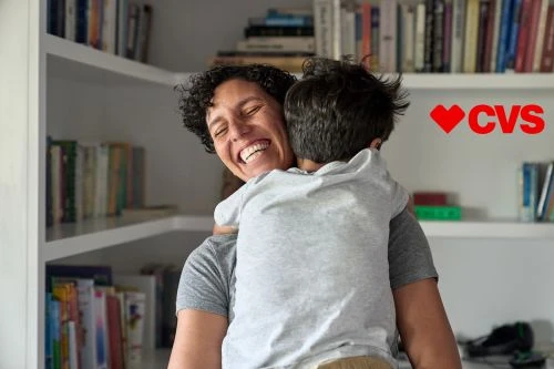 Smiling mother holding her child in an indoor home setting with book shelves in the background with natural lighting during daytime.