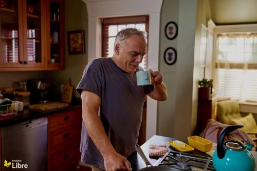 Middle-aged man in a grey t-shirt holding a coffee mug in a home kitchen by photographer Augustus Butera.