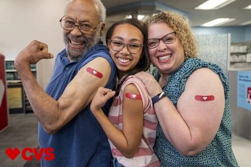 Three people pose indoors, smiling with bandages on their arms, showing their COVID-19 vaccination. CVS logo is visible in corner.