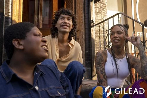 Three smiling people are sitting outside on stairs in casual clothing, captured in a medium shot during the daytime. The Gilead logo is visible.