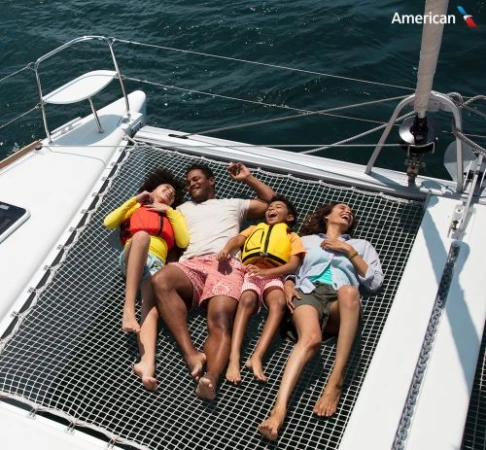 Family of four relaxes on a catamaran over the sea. Adults and children wear life jackets while enjoying a sunny day on the water.
