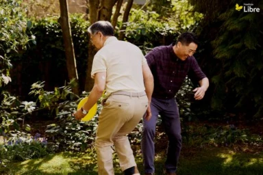 Two middle-aged men playing outdoors in a garden, one holding a yellow disc.