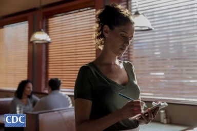 Waitress taking an order writing on a notepad inside a restaurant with wooden blinds