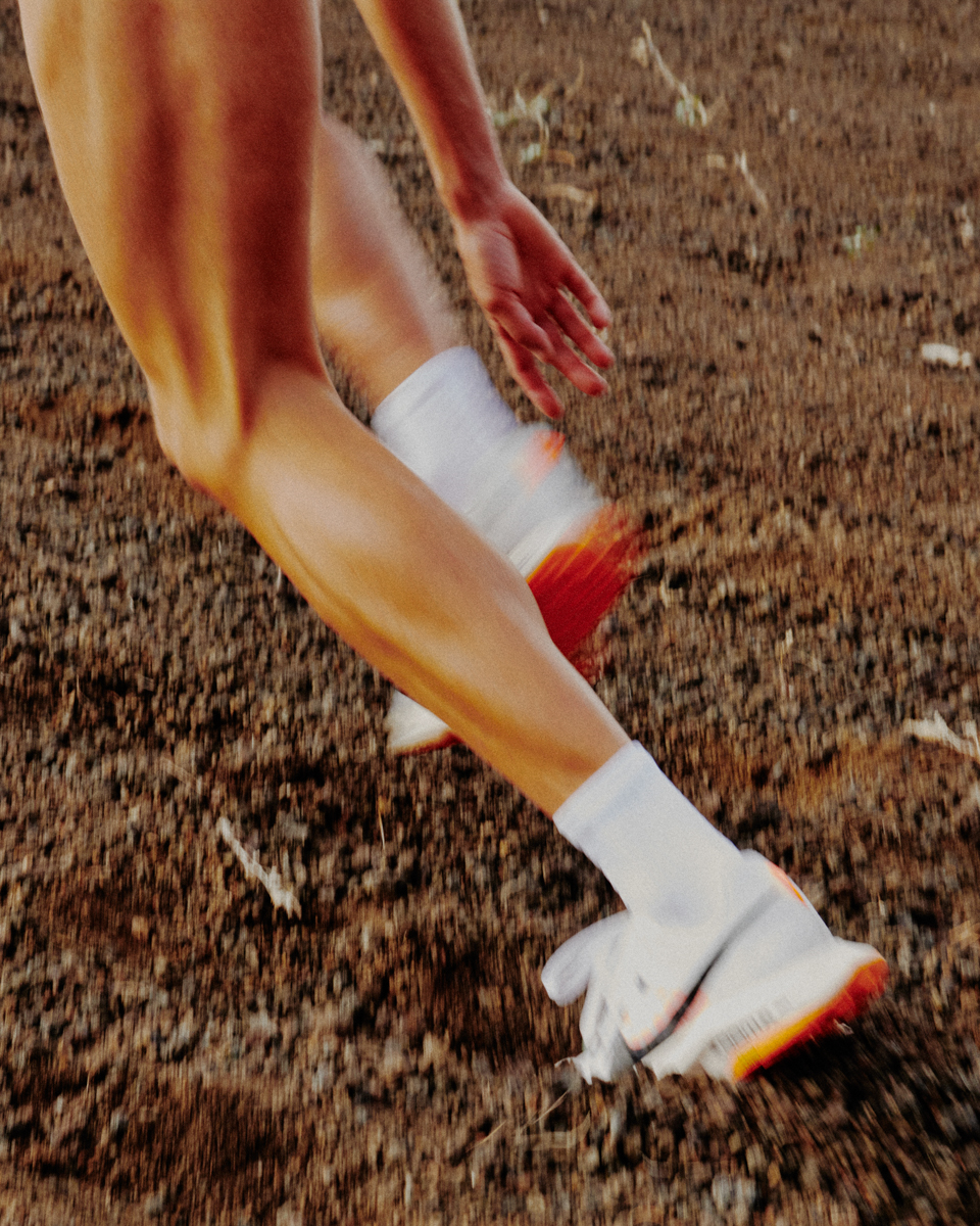 Close up of a runner's legs and feet in motion on a dirt path. The athletic shoes and white socks are visible, suggesting fitness activity.