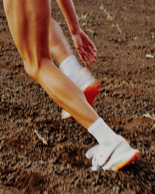 Close up of a runner's legs and feet in motion on a dirt path. The athletic shoes and white socks are visible, suggesting fitness activity.