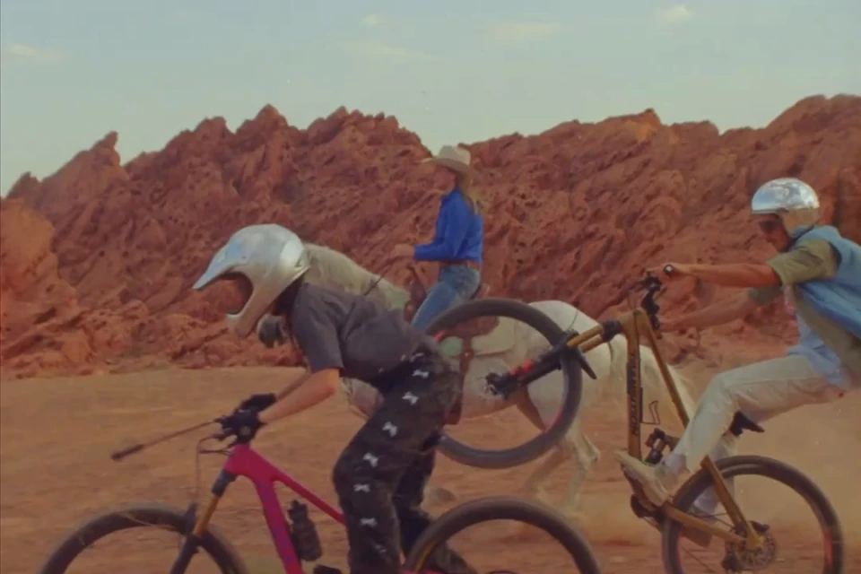 Three people cycling and riding a horse through a desert landscape with red rock formations under a clear sky, active pursuits.