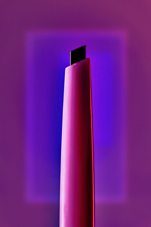 Close-up product shot of a pink eyebrow pencil against a purple background with square lighting, showcasing beauty and makeup tools.