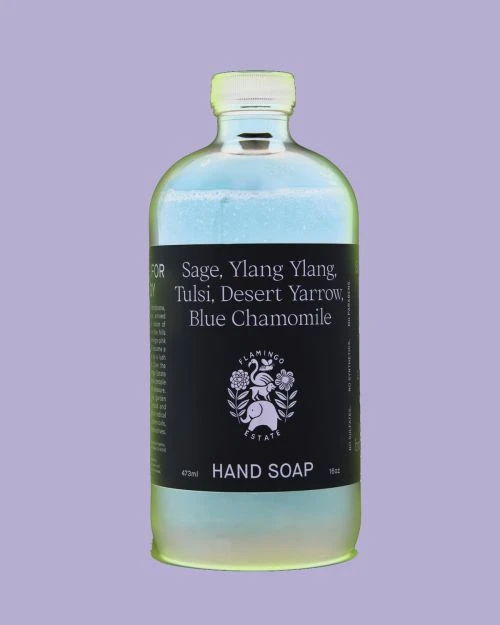 Close-up studio shot of a clear bottle of Flamingo Estate hand soap against a light purple background with the brand name on the label.