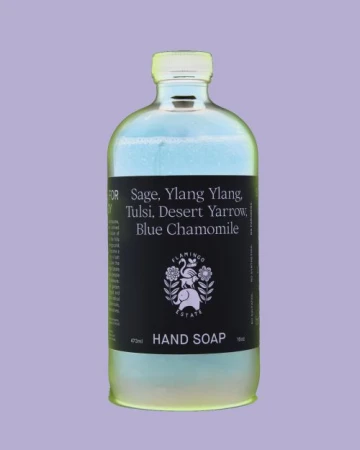 Close-up studio shot of a clear bottle of Flamingo Estate hand soap against a light purple background with the brand name on the label.