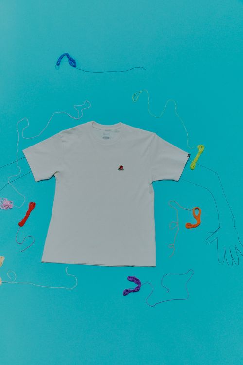 White t-shirt product flat lay on bright blue background with colorful loose embroidery floss and hand outline art. Apparel advertising.
