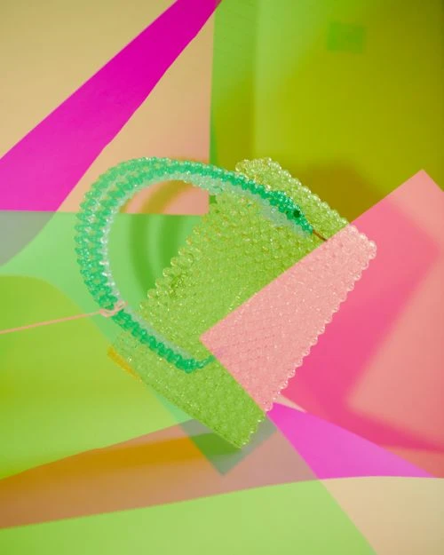 Abstract still life featuring a transparent green beaded object with a pink shape set against layers of pink and green colors.
