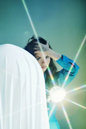 Woman in blue shirt posing with a bright starburst light source and white draped fabric by Frankie Carino