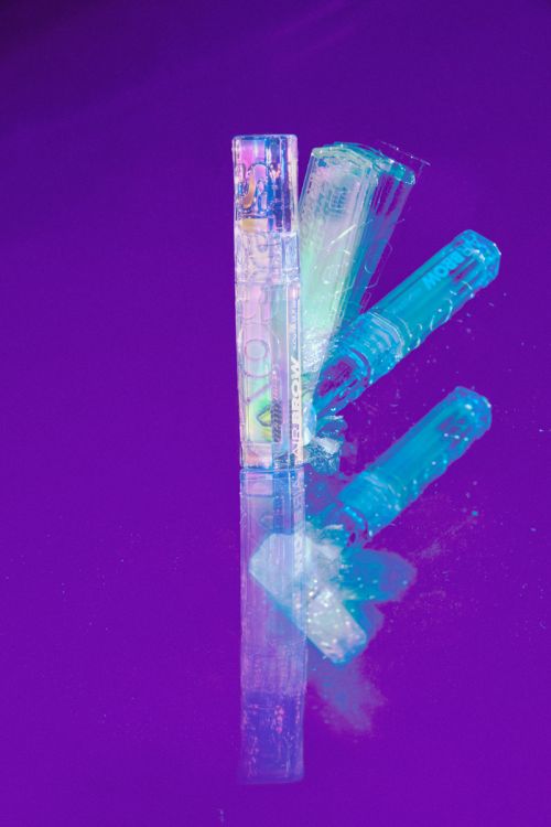 Cosmetic tubes reflecting on a vibrant purple glossy surface with multiple exposures and cyan lighting by Frankie Carino