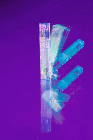 Cosmetic tubes reflecting on a vibrant purple glossy surface with multiple exposures and cyan lighting by Frankie Carino
