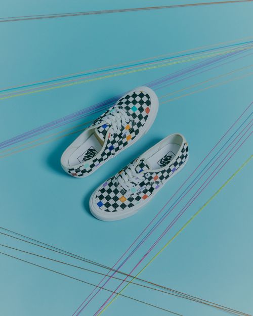 Top-down view of black and white checkerboard canvas sneakers with colorful accents on a pale blue background with colored thread lines