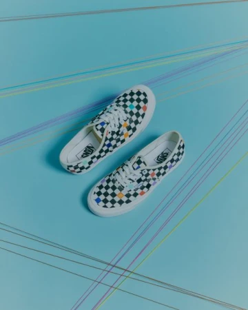 Top-down view of black and white checkerboard canvas sneakers with colorful accents on a pale blue background with colored thread lines