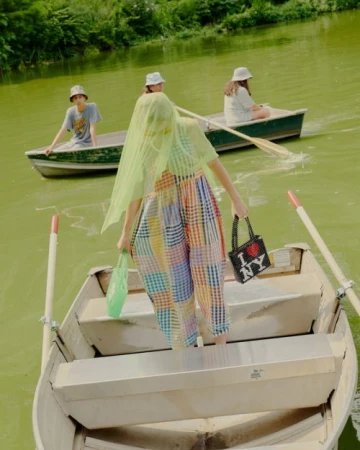 Four people in rowboats on a pond with trees, wearing casual clothing and hats, carrying shopping bags, and enjoying a sunny day outdoors.