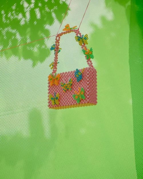 A pink beaded purse with butterfly accents dangles against a bright green background. A novel take on an everyday accessory.