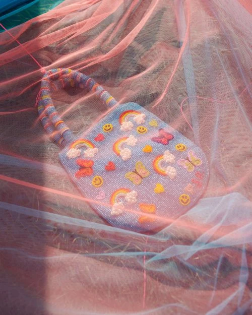 Beaded handbag with rainbow and butterfly designs displayed on a pink tulle surface in an indoor studio setting. Fashion accessory.