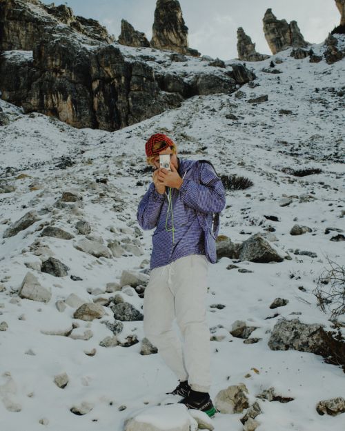 Man in jacket taking a photo on a snow-covered mountain with rock formations. The sky is visible in the background.