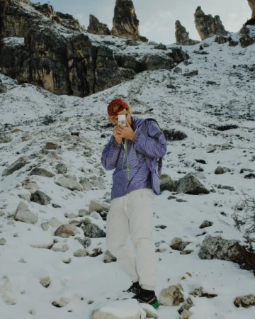 Man in jacket taking a photo on a snow-covered mountain with rock formations. The sky is visible in the background.