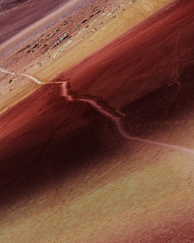 A high-angle shot showcases a vibrant, multicolored mountain terrain crisscrossed by a winding path, creating a visually striking landscape.