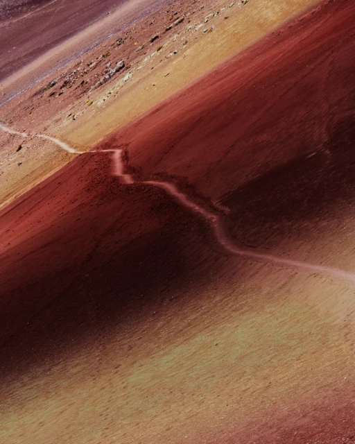 A high-angle shot showcases a vibrant, multicolored mountain terrain crisscrossed by a winding path, creating a visually striking landscape.