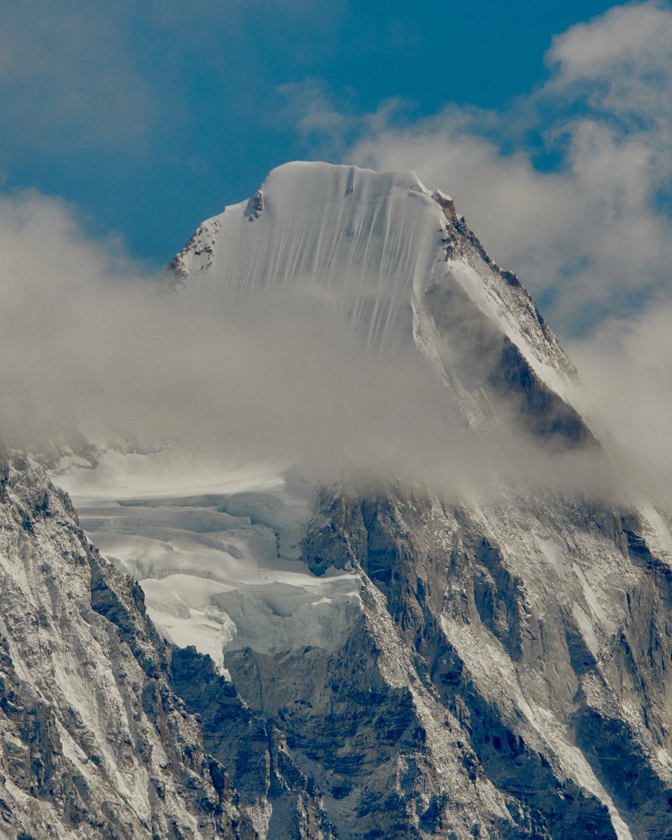 Snow-covered mountain peak surrounded by low-hanging clouds against a blue sky