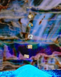 A vertical stack of floating rings suspended above a bright blue mound of sand against a colorful marbled background