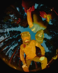 Fisheye low angle view of two mountain bikers in helmets and protective gear looking down inside a forest.