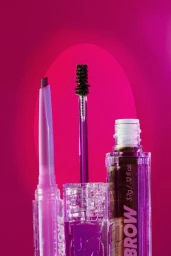 Close-up product photography of three eyebrow makeup items against a vibrant pink gradient background by Frankie Carino.