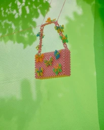 Pink beaded handbag with colorful butterfly motifs hanging against a vibrant green mesh background.