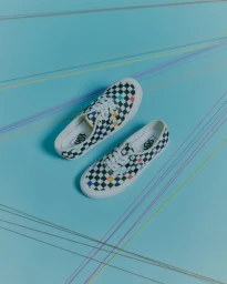 Top-down view of black and white checkerboard canvas sneakers with colorful accents on a pale blue background with colored thread lines