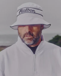 Man wearing a white bucket hat with dark text and a white quarter zip sweatshirt outdoors