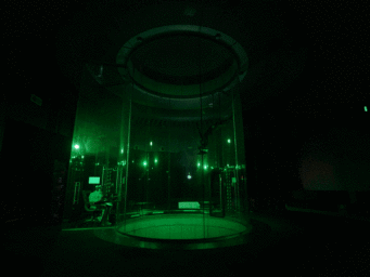 A person skydiving inside a vertical wind tunnel illuminated by green light, photographed by Frankie Carino.