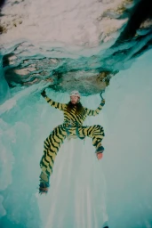 Ice climber in a yellow and black striped suit scaling a vibrant turquoise glacier cave wall