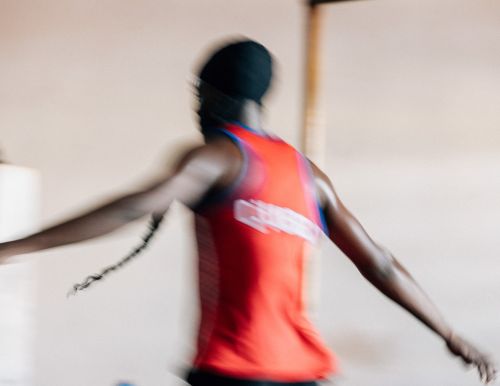 Motion blur of an adult Black man wearing a red sleeveless shirt and a black cap indoors.