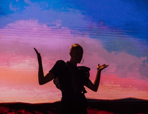 Person in silhouette with arms raised against a backdrop of gradient pink and blue colors, creating a dynamic visual contrast.