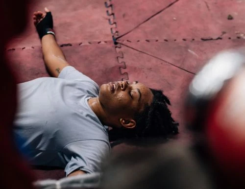 Athlete in sports attire lies exhausted on a pink wrestling mat, showcasing dedication and the physical demands of athletic training.
