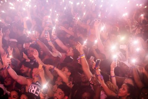 Large crowd of people holding up phones with flashlights in a dark venue at a concert or event, creating a vibrant and energetic atmosphere.