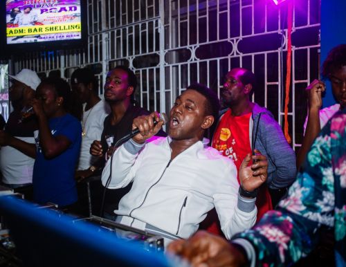 Singer performs on stage with microphone at an indoor music event, backed by a keyboard and band, under bright stage lighting.