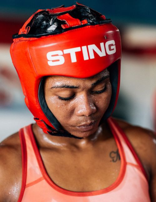Close-up of a female boxer wearing a red headgear with the word 'STING' in white letters, looking down with a serious expression.
